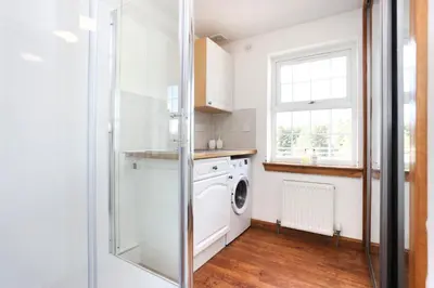 a laundry room with a washing machine and a window at JOIVY Greenknowes Farmhouse with Hot Tub and Bar in Kelty