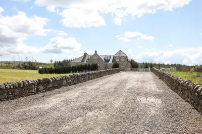 a dirt road in front of a house with a stone wall at JOIVY Greenknowes Farmhouse with Hot Tub and Bar in Kelty
