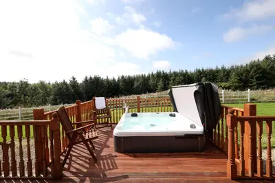 a hot tub sitting on a deck with two chairs at JOIVY Greenknowes Lodge with Hot Tub and Wood Burning Stove in Kelty