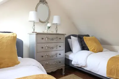 a bedroom with two beds and a dresser with a mirror at JOIVY Greenknowes Lodge with Hot Tub and Wood Burning Stove in Kelty