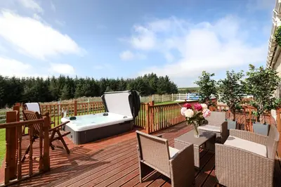 a deck with a hot tub and chairs on it at JOIVY Greenknowes Lodge with Hot Tub and Wood Burning Stove in Kelty