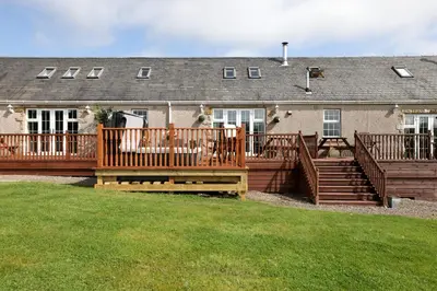 a large deck with wooden railings in front of a house at JOIVY Greenknowes Lodge with Hot Tub and Wood Burning Stove in Kelty