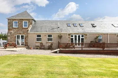 a house with a wooden deck and a patio at JOIVY Greenknowes Estate with Hot Tub and Bar - Farmhouse and Lodge in Kelty