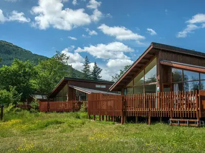 a house in a field with mountains in the background at Ardgartan Argyll Cabins - Forest Holidays in Arrochar