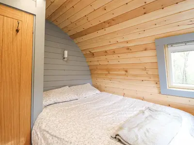 a bed in a room with a wooden wall at Elleric Pods - The Last Resort in Appin
