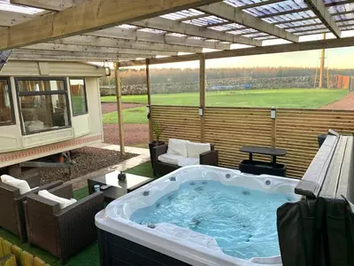 a hot tub on a patio with a view of a field at North Lodge Holiday Home, Hot Tub & Sauna in Carnwath