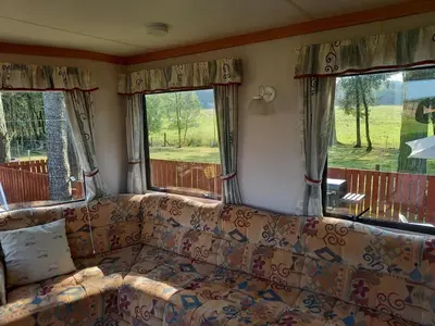 a couch in a living room with two windows at North Lodge Holiday Home, Hot Tub & Sauna in Carnwath