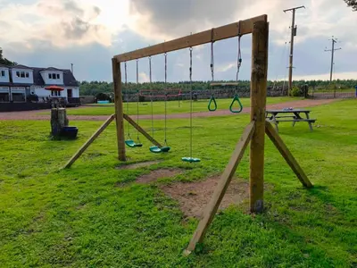 an empty playground with swings and a picnic table at North Lodge Holiday Home, Hot Tub & Sauna in Carnwath