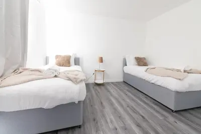 two beds in a bedroom with white walls and wood floors at Renfrew House in Renfrew