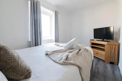 a white bedroom with a bed and a tv at Renfrew House in Renfrew