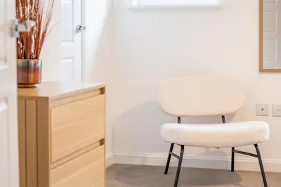 a white chair sitting next to a wooden cabinet at Lendrick House-Spacious 3 Bed House in Falkirk in Polmont