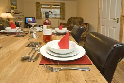 a dining room table with plates and a bottle of wine at Clan Cottages Luxury Thatched Retreat near Oban in Oban