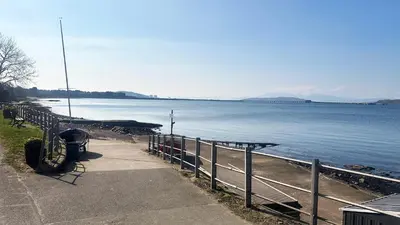 a bench next to a fence next to a body of water at Bay View Cottage in Fairlie