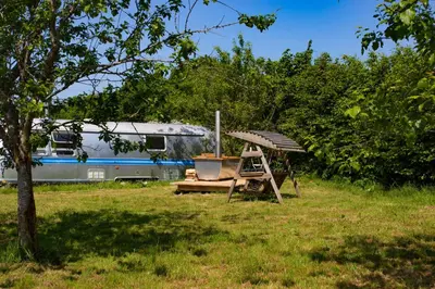 a chair and a table in a field with a train at Luxury Airstream Getaway with Sauna and Hot Tub in Gartness