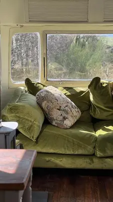 a green couch with pillows sitting in front of a window at Luxury Airstream Getaway with Sauna and Hot Tub in Gartness