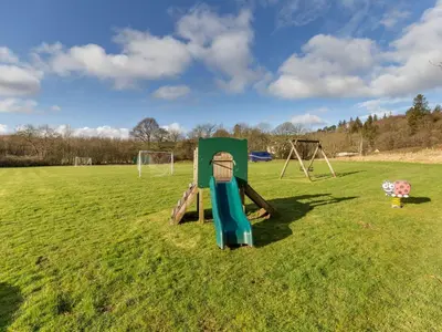 a playground in a field with a swing set at Holiday Home Foxglove cottage by Interhome in Straiton