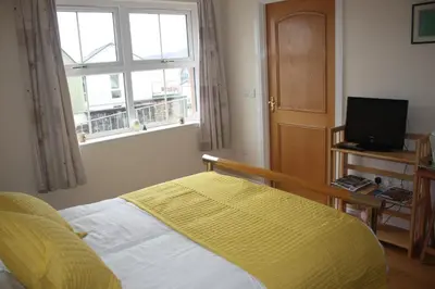 a bedroom with a bed with a yellow blanket and a window at Stonewater House Vegan Bed and Breakfast in Lamlash