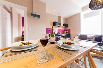 a table with a glass of wine and plates of food at The Spires Serviced Apartments Edinburgh in Edinburgh