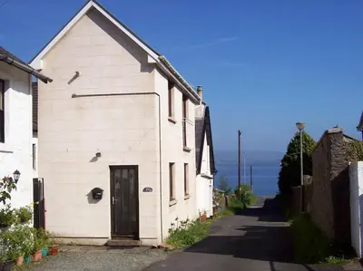 a white building with a door on the side of a street at The Snug a cosy, quirky detached cottage with sea views in Innellan