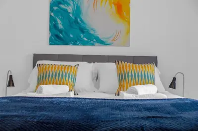 a bedroom with a bed with two pillows and a painting at Arran Cottage - 4 Bed Home on M8 in Coatbridge