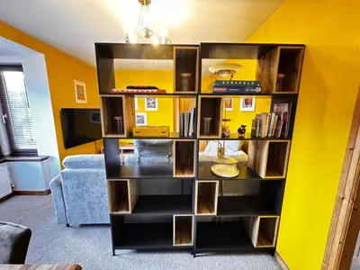 a book shelf in a living room with a yellow wall at The Maltings Retreat in Inverkeithing