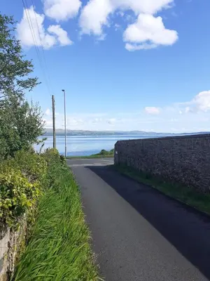 a road next to a wall next to the ocean at Coach House Cottage a cosy, detached hideaway with garden, nr the sea in Innellan