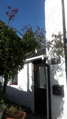 a white house with a black door and a street sign at Coach House Cottage a cosy, detached hideaway with garden, nr the sea in Innellan