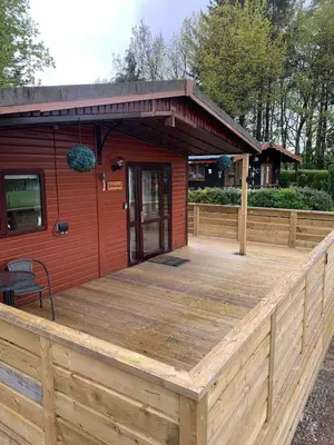 a large wooden deck with a red building at The Woodhouse Cabin 8 in Moffat