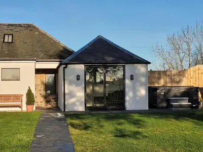 a white house with glass doors on a yard at Hot Tub Cottage in Ayrshire in Stewarton