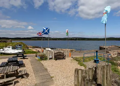 a park with benches and flags next to a body of water at Coastal Charm in Kingarth