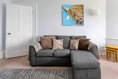 a living room with a gray couch with pillows at Coastal Charm in Kingarth