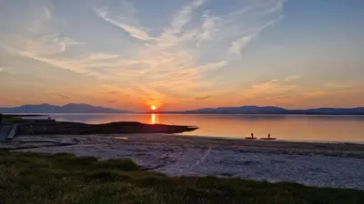 a sunset over the water with two people on the beach at Lerags glen farm pods in Lerags