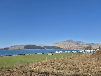 a field next to a body of water with houses at The Hideouts at Port nan Gael Campsite in Pennyghael