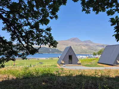 a small house in a field next to a body of water at The Hideouts at Port nan Gael Campsite in Pennyghael