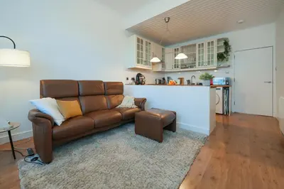 a living room with a brown leather couch and a kitchen at Central 1-bed flat - Walk to shops, pubs and station in Saltcoats