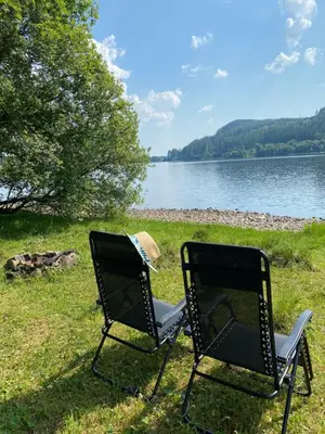 two chairs sitting in the grass next to a lake at The Hidden Shepherds Hut- Off Grid Retreat in Castle Douglas