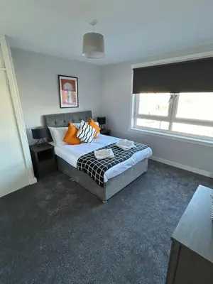 a bedroom with a bed with orange pillows and a window at 3-Bed Apartment Central Greenock in Greenock
