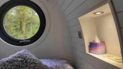 a bedroom with a round window and a bed with a pillow at Squirrels Wood Lodge, nr Glencoe, dog friendly in Acharra