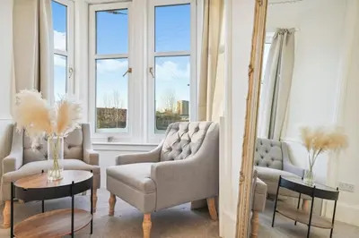 a living room with two chairs and a couch and windows at Large Terraced Home with Parking in Glasgow