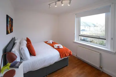 a bedroom with a bed with an orange blanket and a window at Barassie Villa located near Troon in Troon
