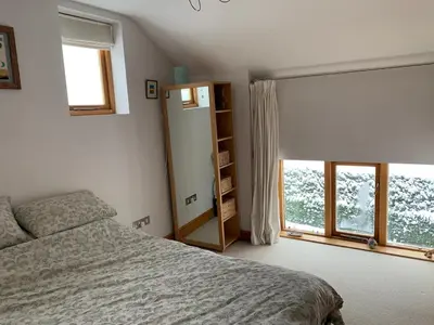 a bedroom with a bed and a book shelf and two windows at Tan Y Bedw Barn in Moffat