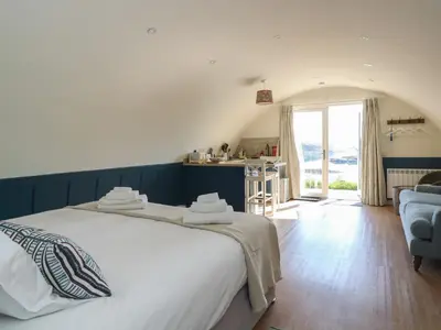 a bedroom with a large white bed and a kitchen at Torsa in Oban