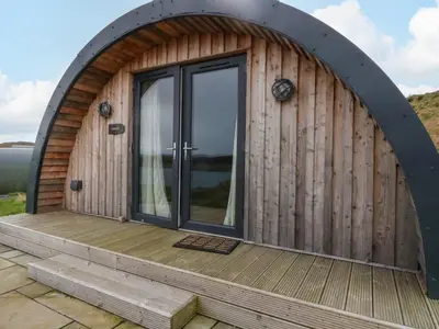 an arched wooden building with a glass door on a deck at Creags in Oban