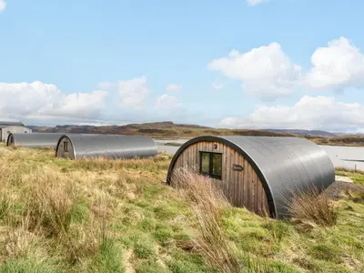 a group of circular buildings in a field with a body of water at Insh in Oban
