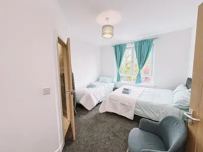 a bedroom with two beds and a chair and a window at Itohan 3-bed Cottage Flat in Glasgow