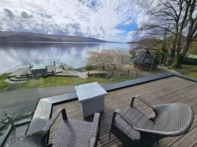 two chairs on a deck with a view of a lake at Fyne Edge - A Luxurious Lochside Haven in Minard