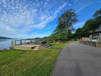 a walkway next to a lake with a house at Fyne Edge - A Luxurious Lochside Haven in Minard