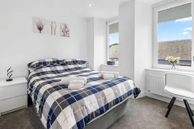 a bedroom with a bed and a chair and windows at Modern & Central 1BR Flat with Sky TV in Oban