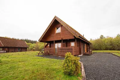 a large wooden cabin with a bench in front of it at Lodge 3 in Stirling