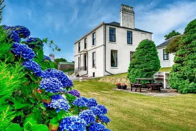 a white house with a picnic table and blue flowers at Rosemount in Campbeltown